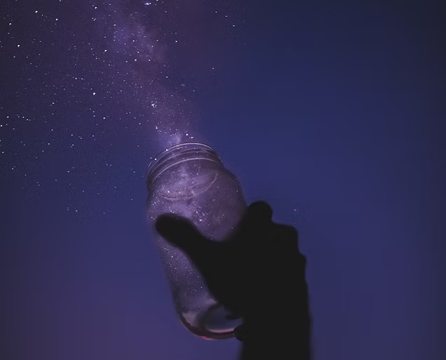 Mão segurando um frasco sob um céu estrelado em tons violeta